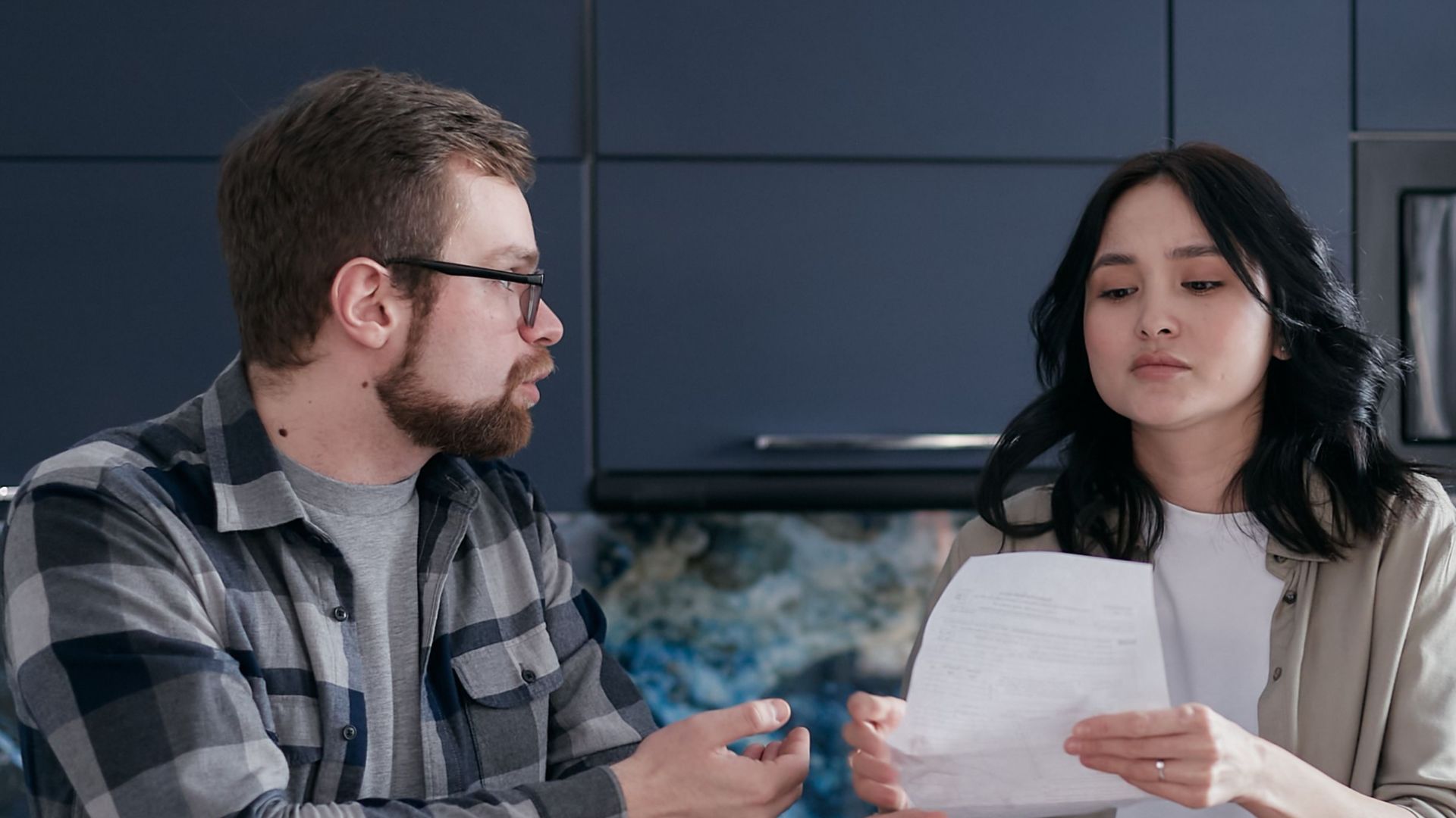 A couple reviews financial documents together at home, focusing on budgeting and bills.