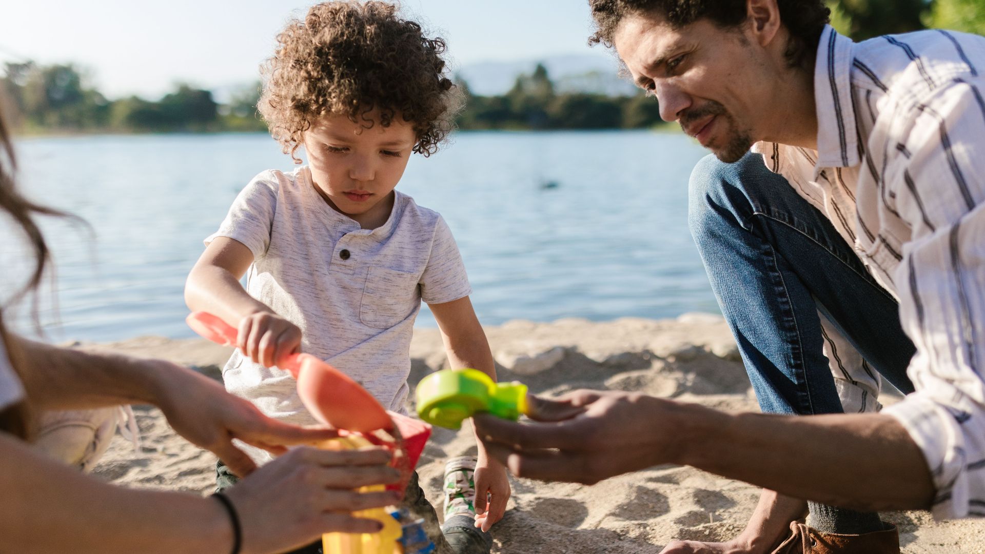 Father and son enjoying playtime with sand toys at the beach on a sunny day.