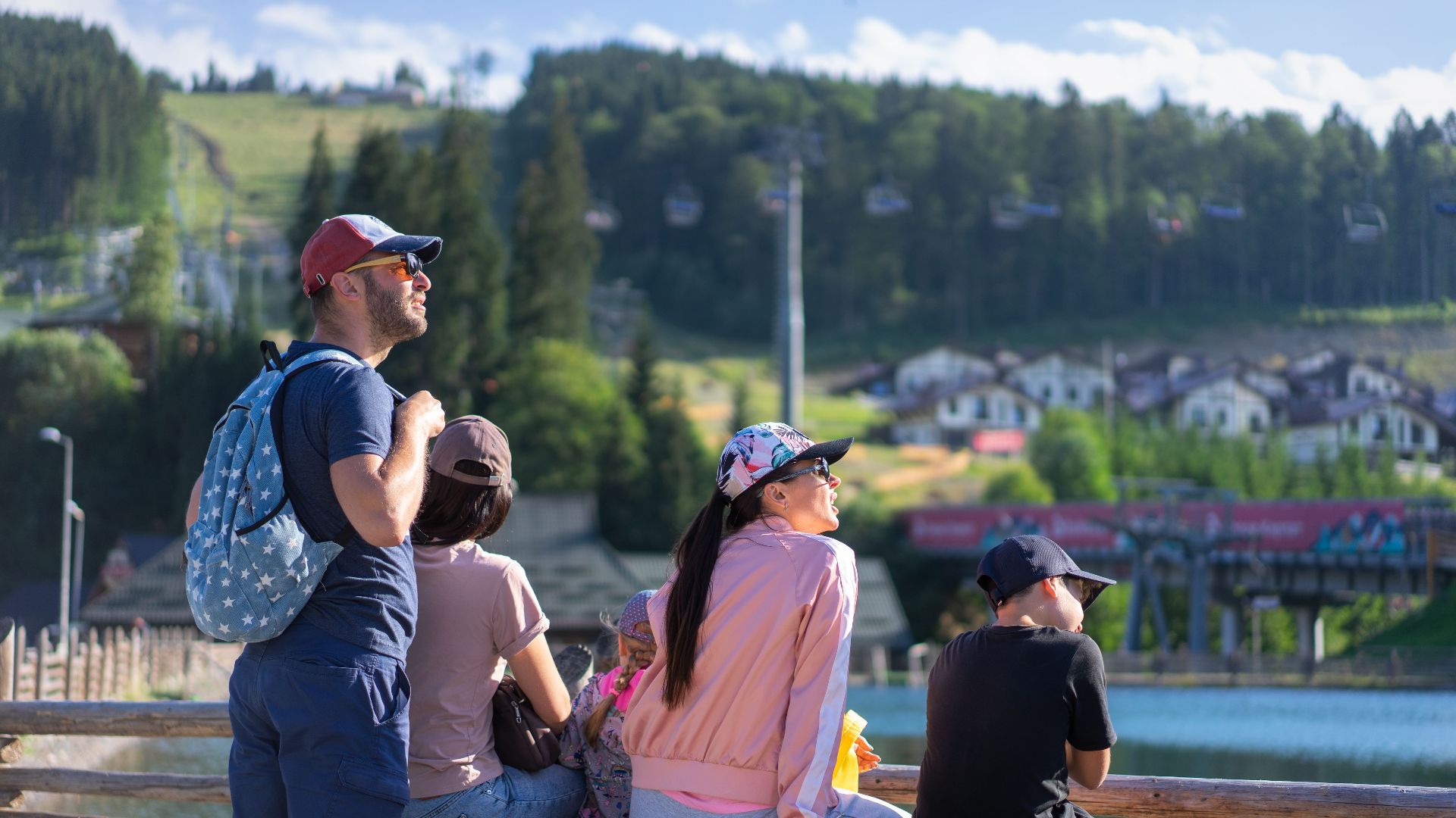 A family enjoys a sunny day sitting on a bench in Bukovel, Ukraine, with scenic mountain views.