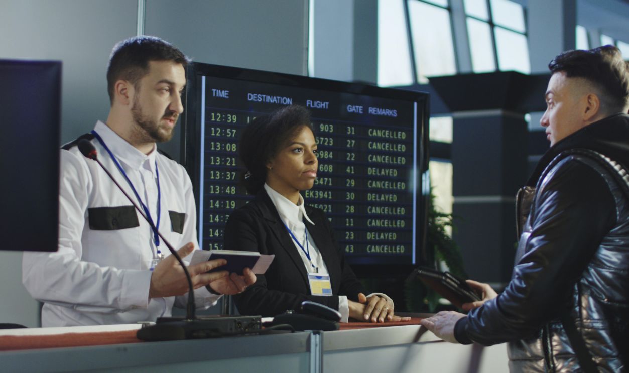 Man giving fingerprints with sensor when passing special control point in airport with employee watching at screen.