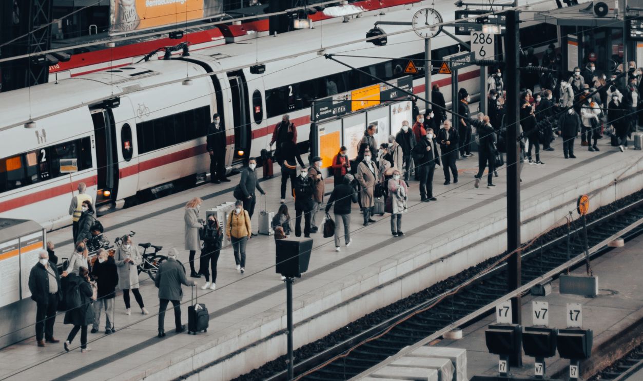 A bustling train station with commuters boarding and alighting trains under an arched roof