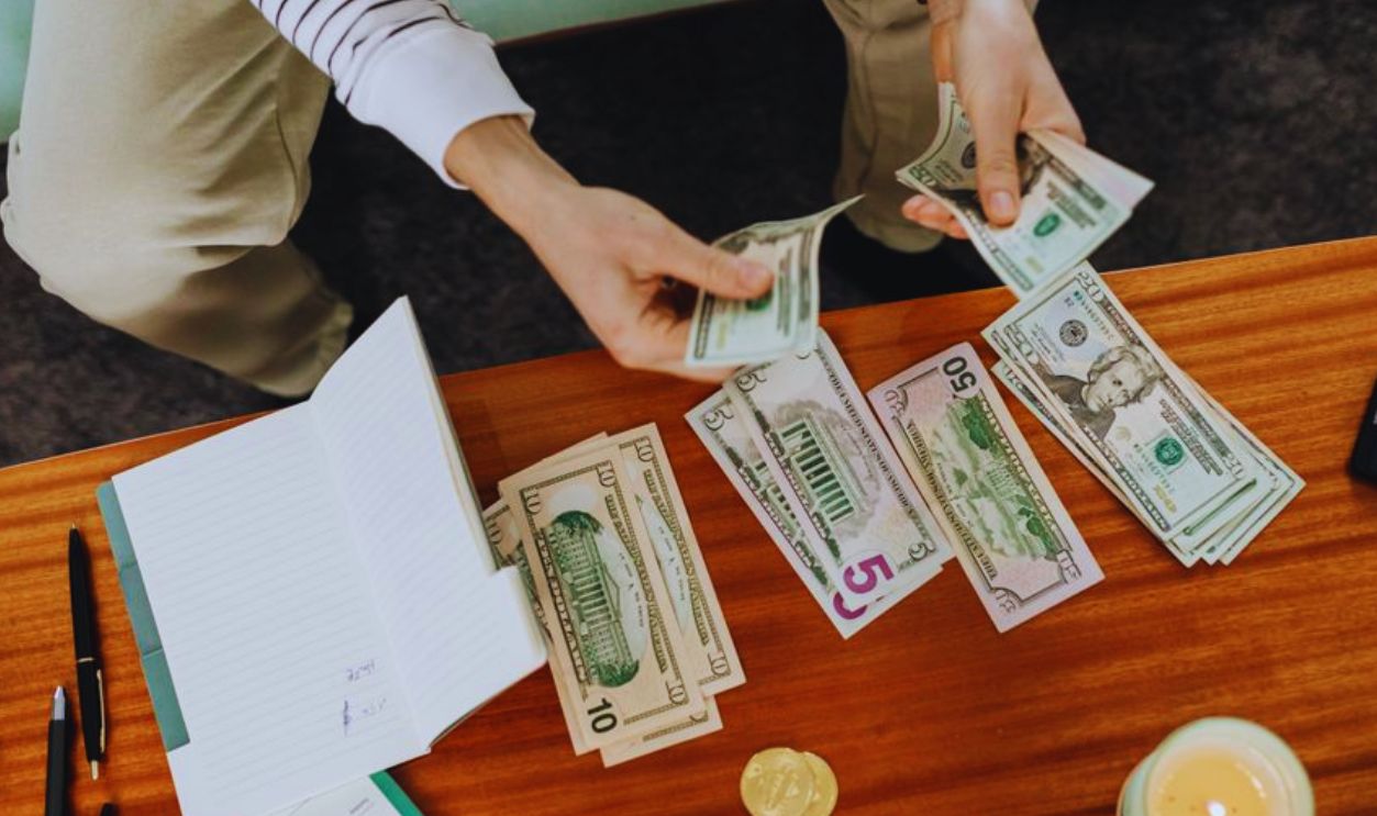 A person sitting and counting various US dollar bills at a table indoors