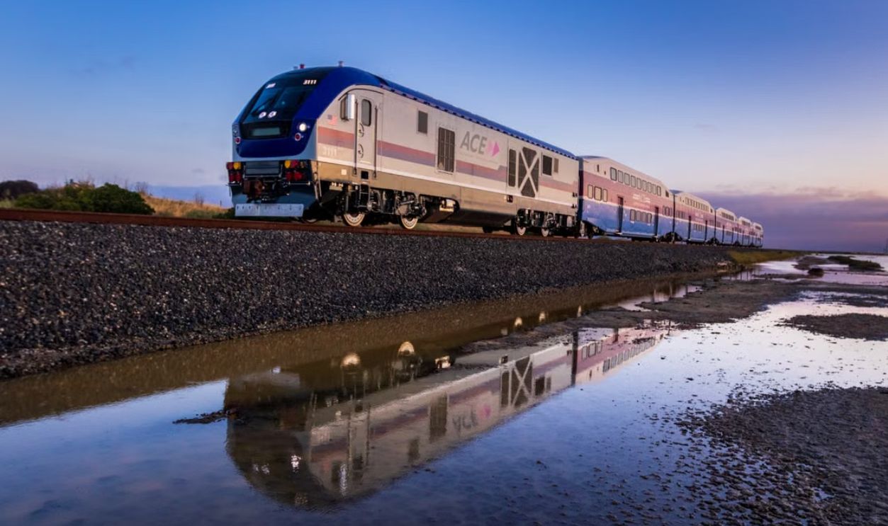 A high-speed train reflected in water at sunrise creates a serene transportation scene
