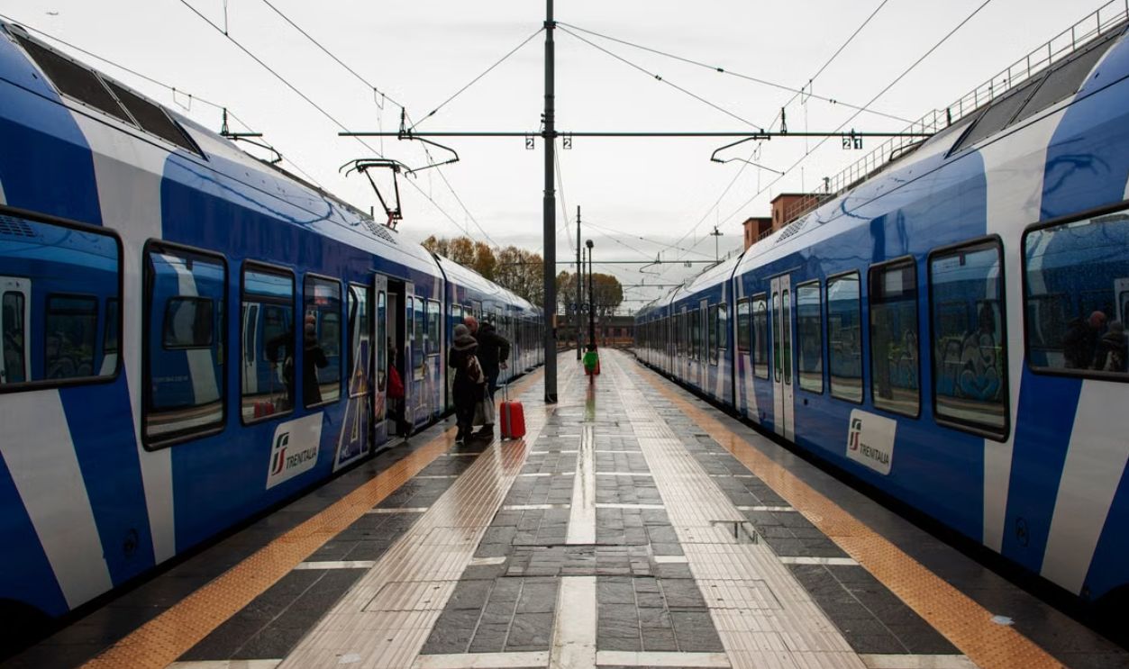 A symmetrical view of a railway platform with Trenitalia trains at a station with passengers boarding