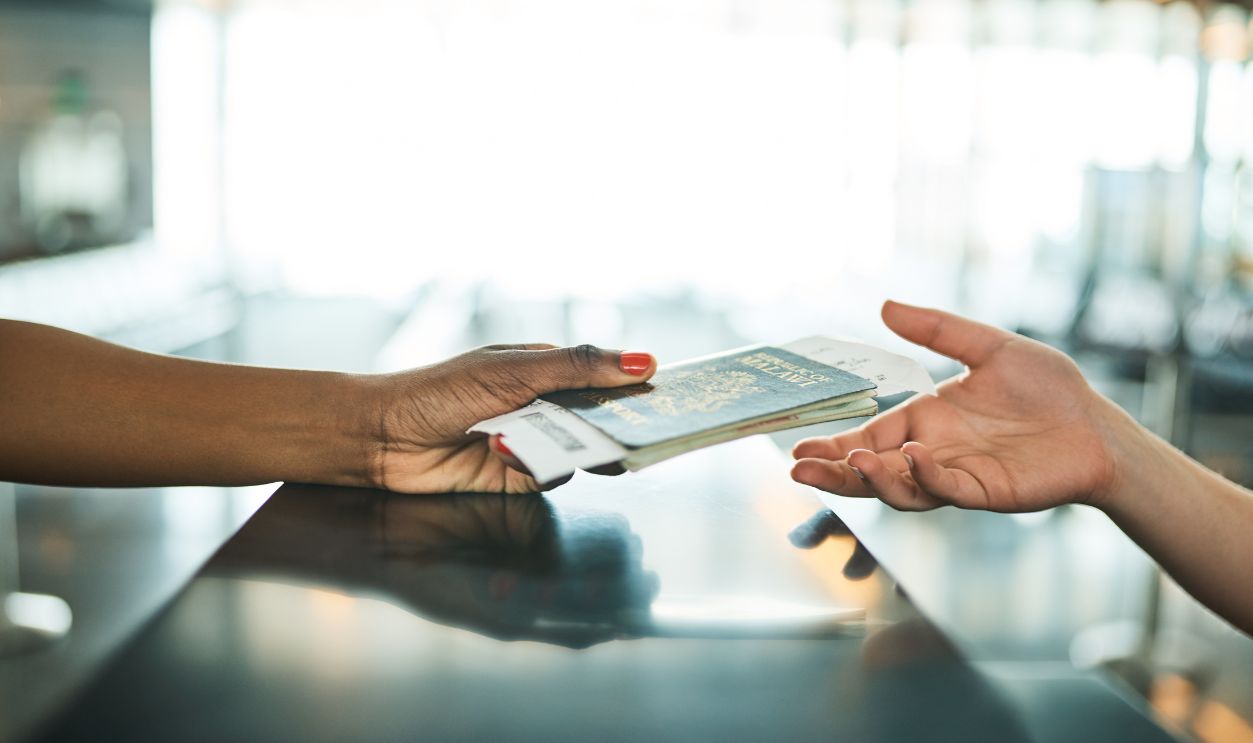 Hands, passport and airport service counter closeup or boarding flight, support and travel desk consultant. Travelling agent, checkin and person help traveller with id book, ticket and safe journey
