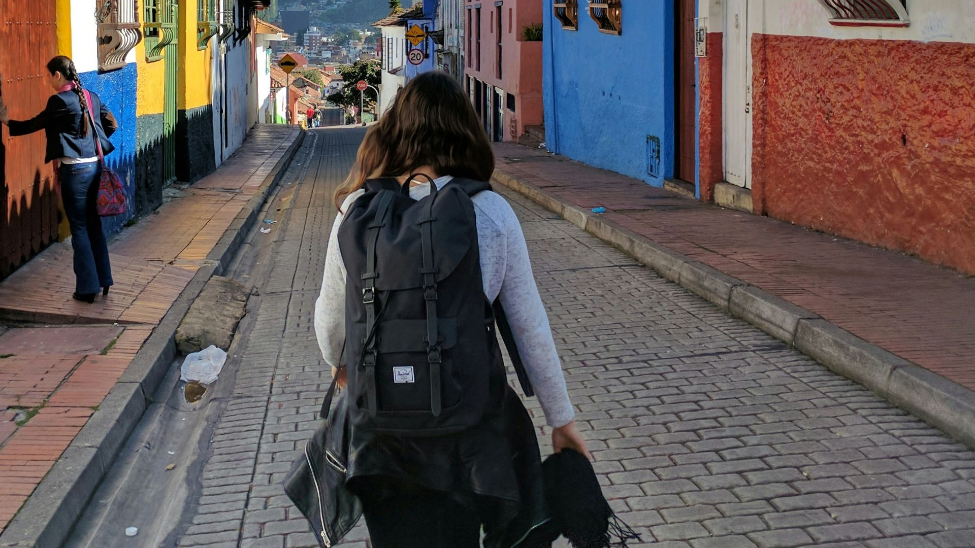 person in gray shirt with backpack walking on street between houses