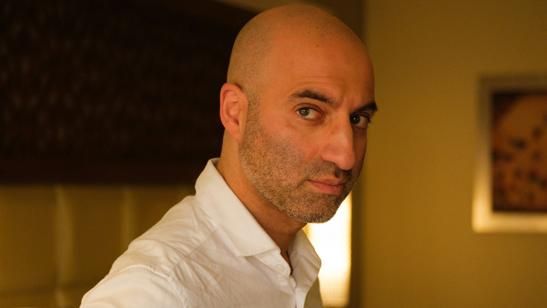Bald man in a white shirt looking at the camera.