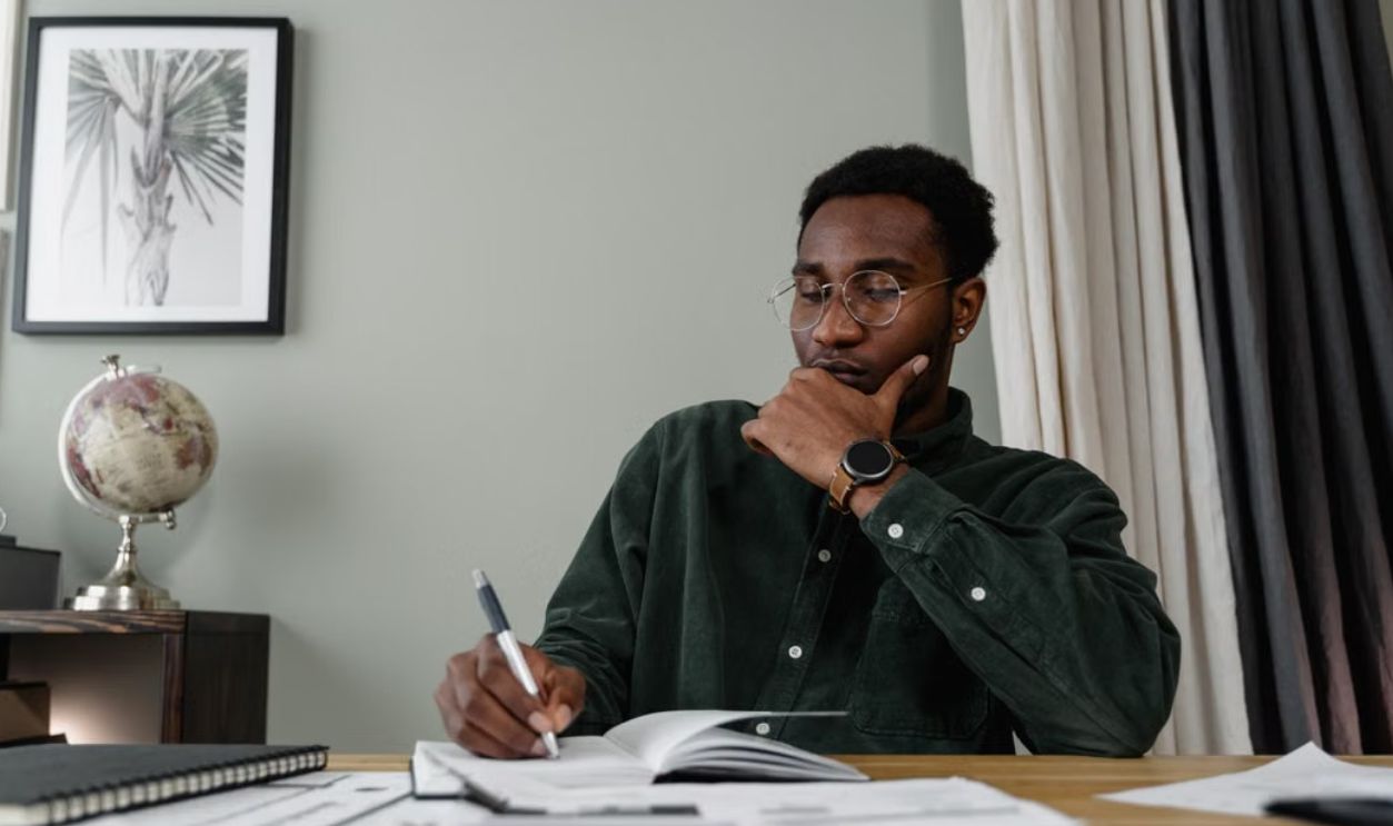 Black man in glasses concentrating over documents at a wooden desk, office setting