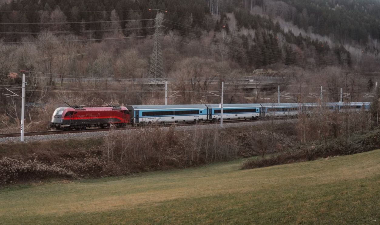 A picturesque red train travels through serene forest landscape, perfect for travel enthusiasts