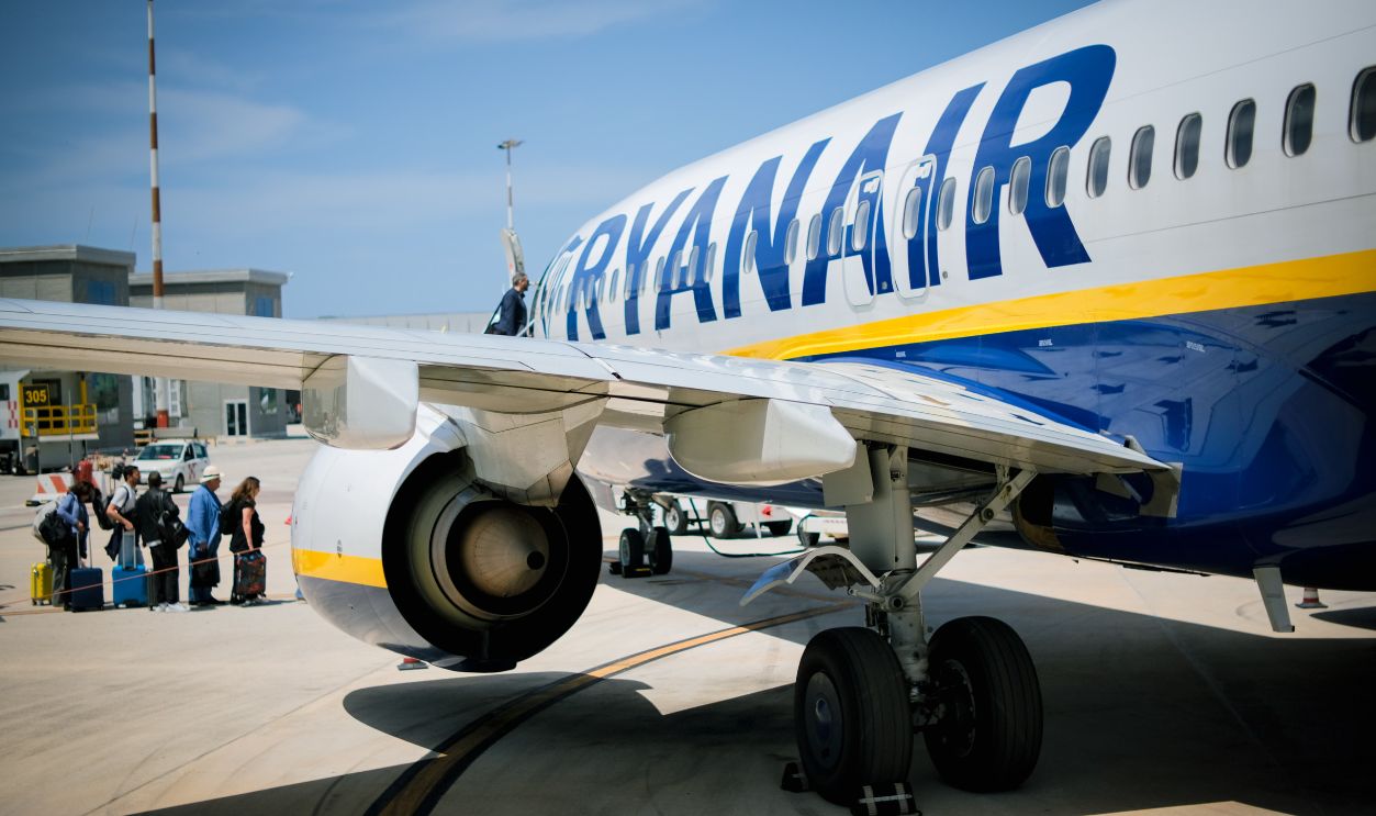 Passengers boarding a Ryanair plane on a sunny day at a Sicilian airport