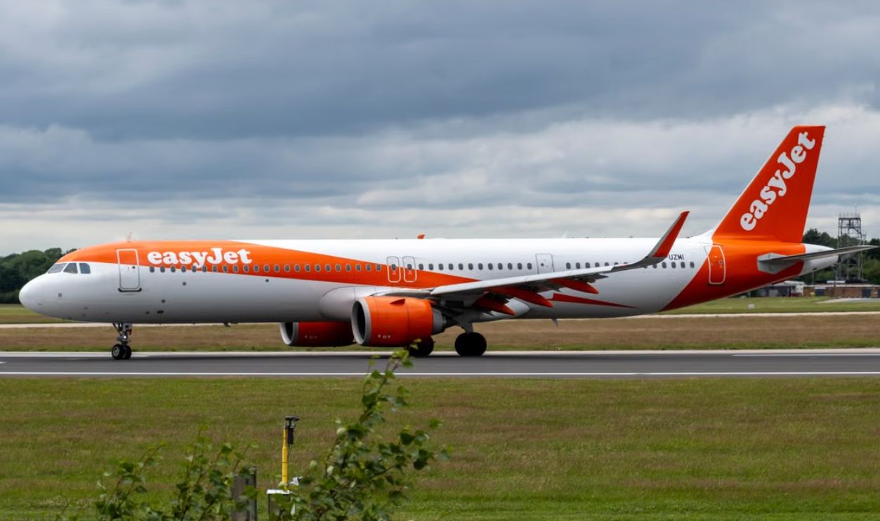 Side view of EasyJet Airbus A321 taxiing on runway under cloudy skies
