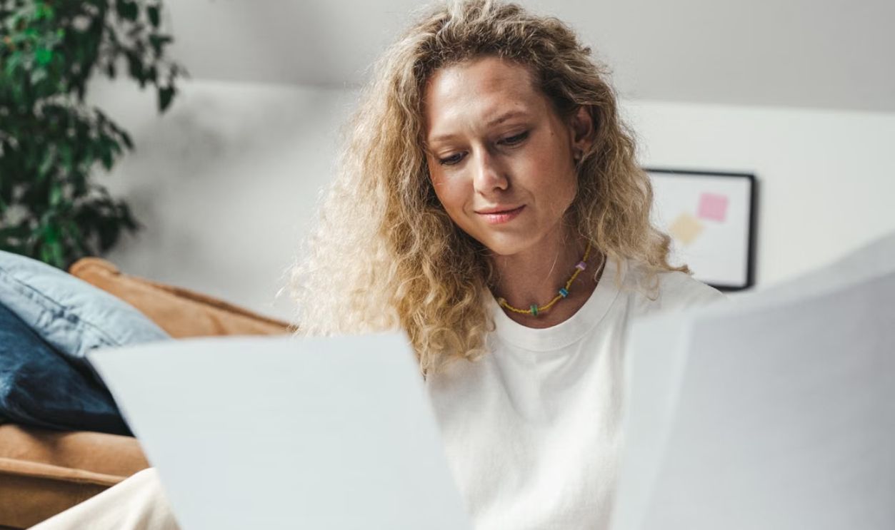 A woman with curly blonde hair analyzing papers while sitting indoors, conveying focus and determination