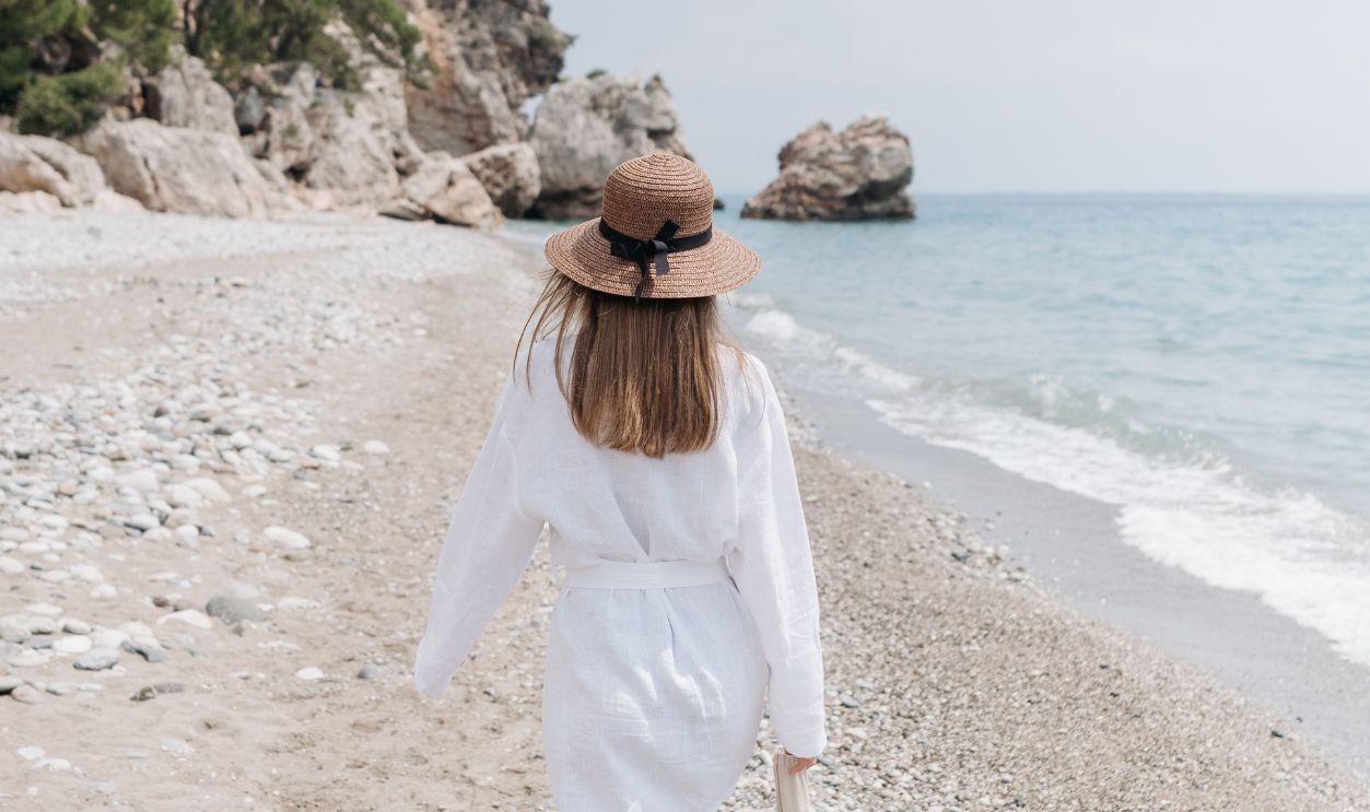 A woman in a white dress and hat strolls by the serene seaside