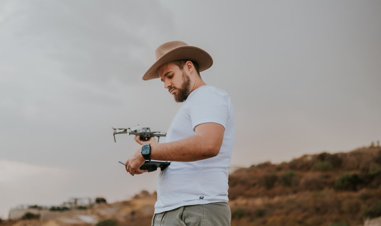 A man with a hat operating a drone outdoors during a cloudy day