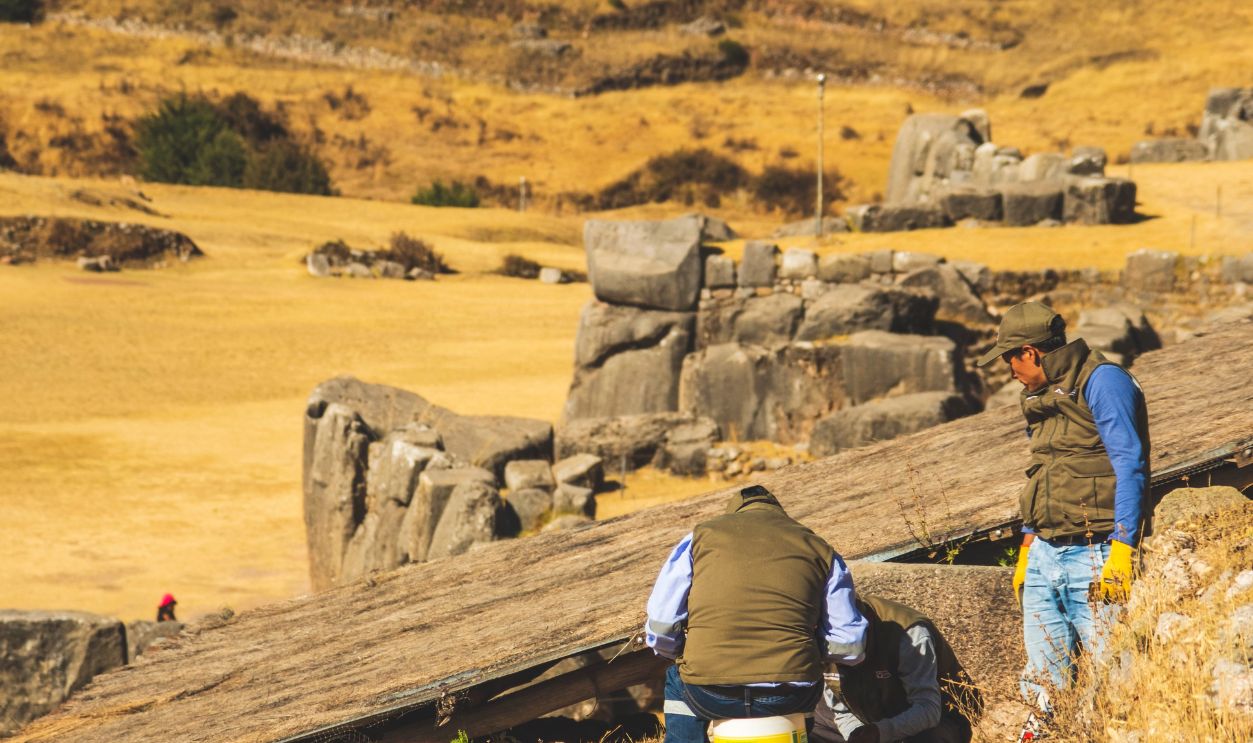 Archaeologists working on restoration in Cuzco ruins under sunny skies, surrounded by scenic landscapes
