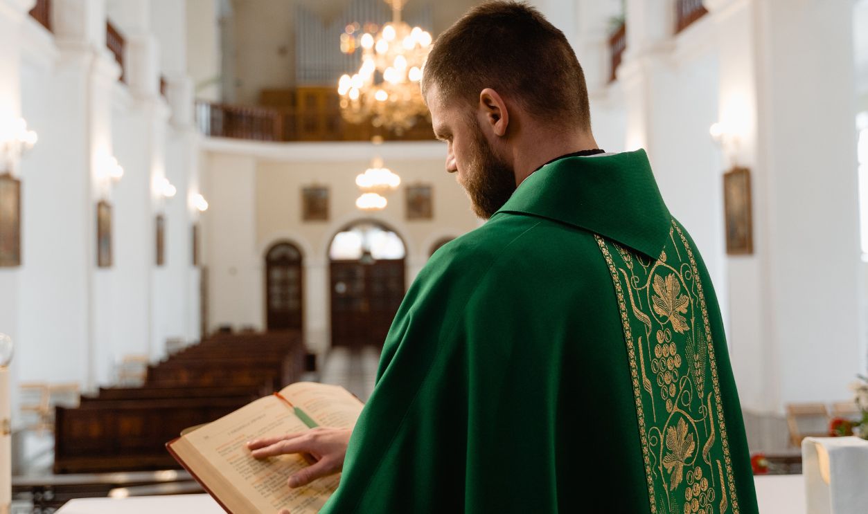 A priest in green vestment reading during a religious service in a grand cathedral
