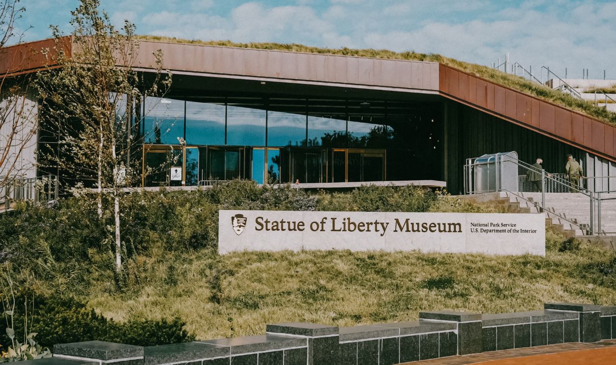 The modern Statue of Liberty Museum surrounded by lush green plants under a clear blue sky
