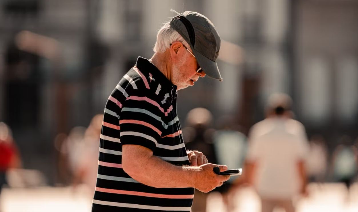 Senior man in striped shirt using smartphone in sunny La Coruna street