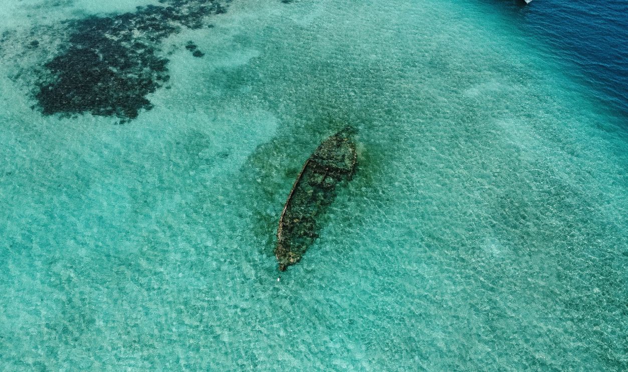 Aerial view captures a sunken ship in clear, turquoise waters, highlighting the ocean's beauty and mystery