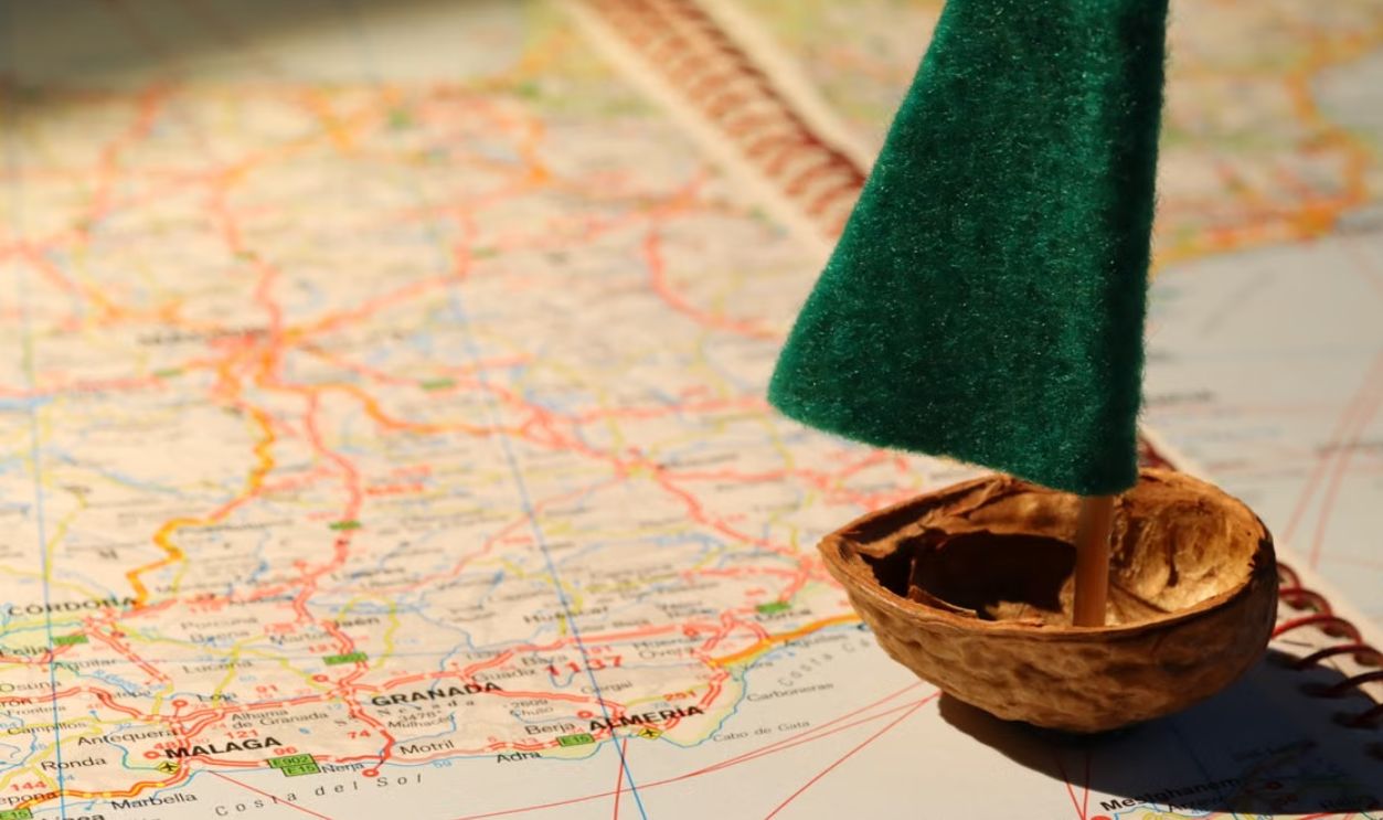 Creative travel metaphor with a tiny sailboat on a detailed world map