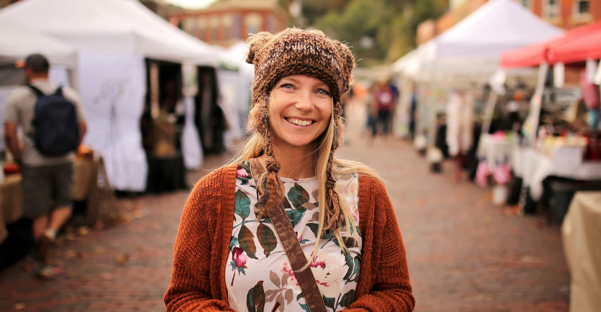 A happy women wearing a hand knit fox winter hat is smiling as she shops outside at a small town fall festival market.