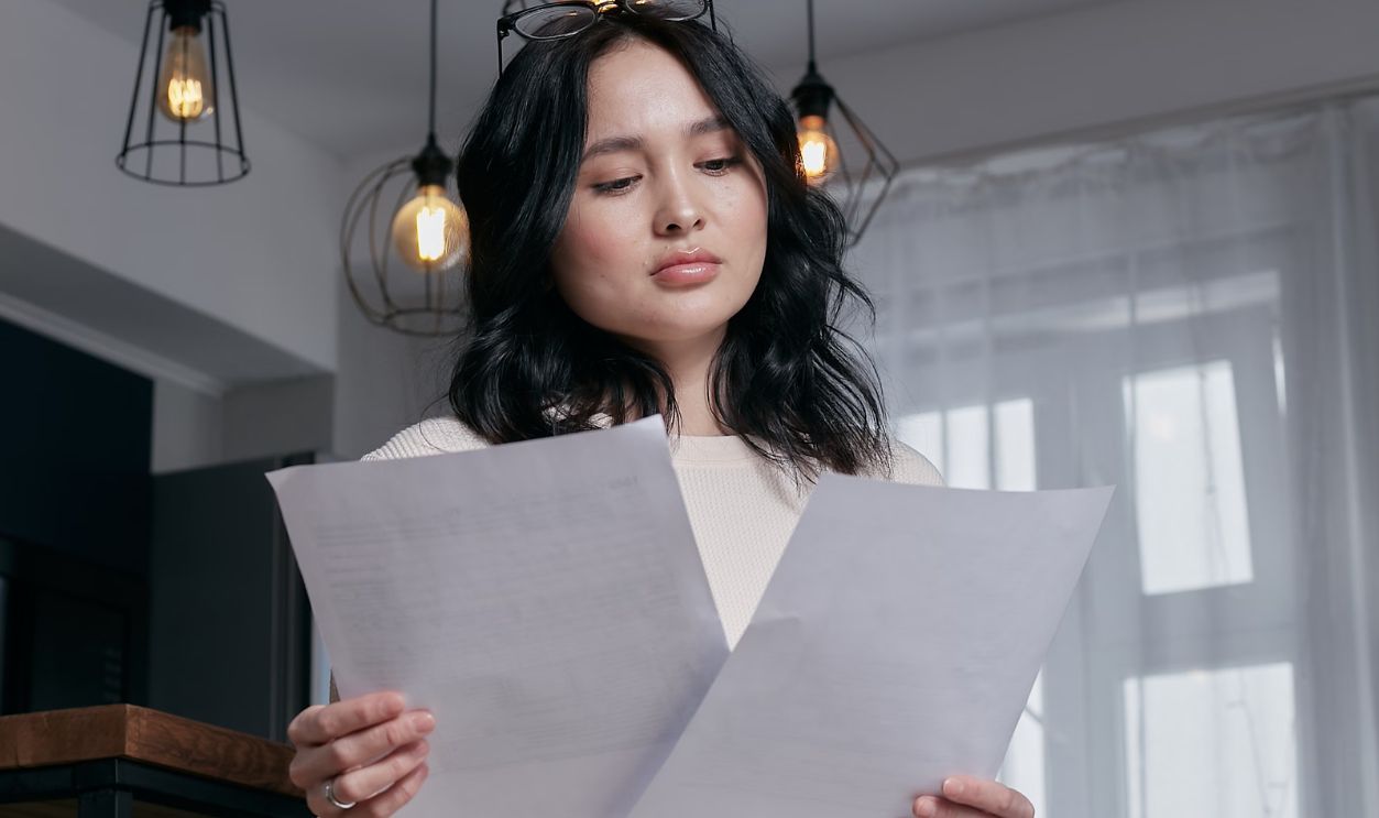 A woman sitting indoors, carefully reviewing papers under a stylish lighting setup