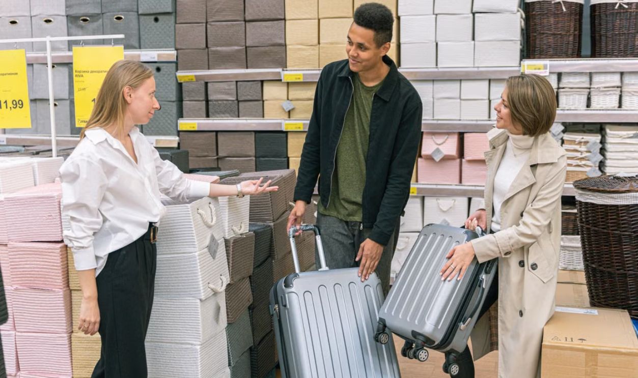 Couple interacting with store assistant while selecting suitcases in a retail store.