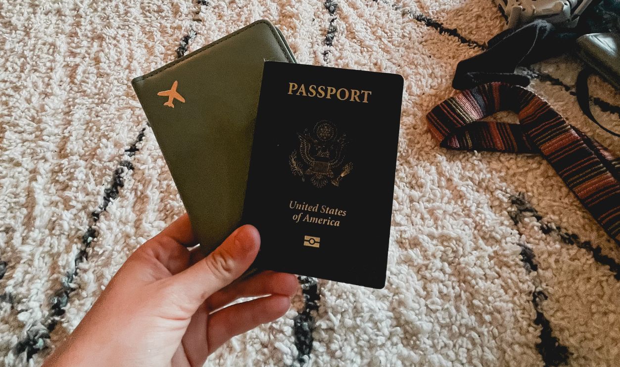 Hand holding two passports on a patterned carpet indoors, travel essentials