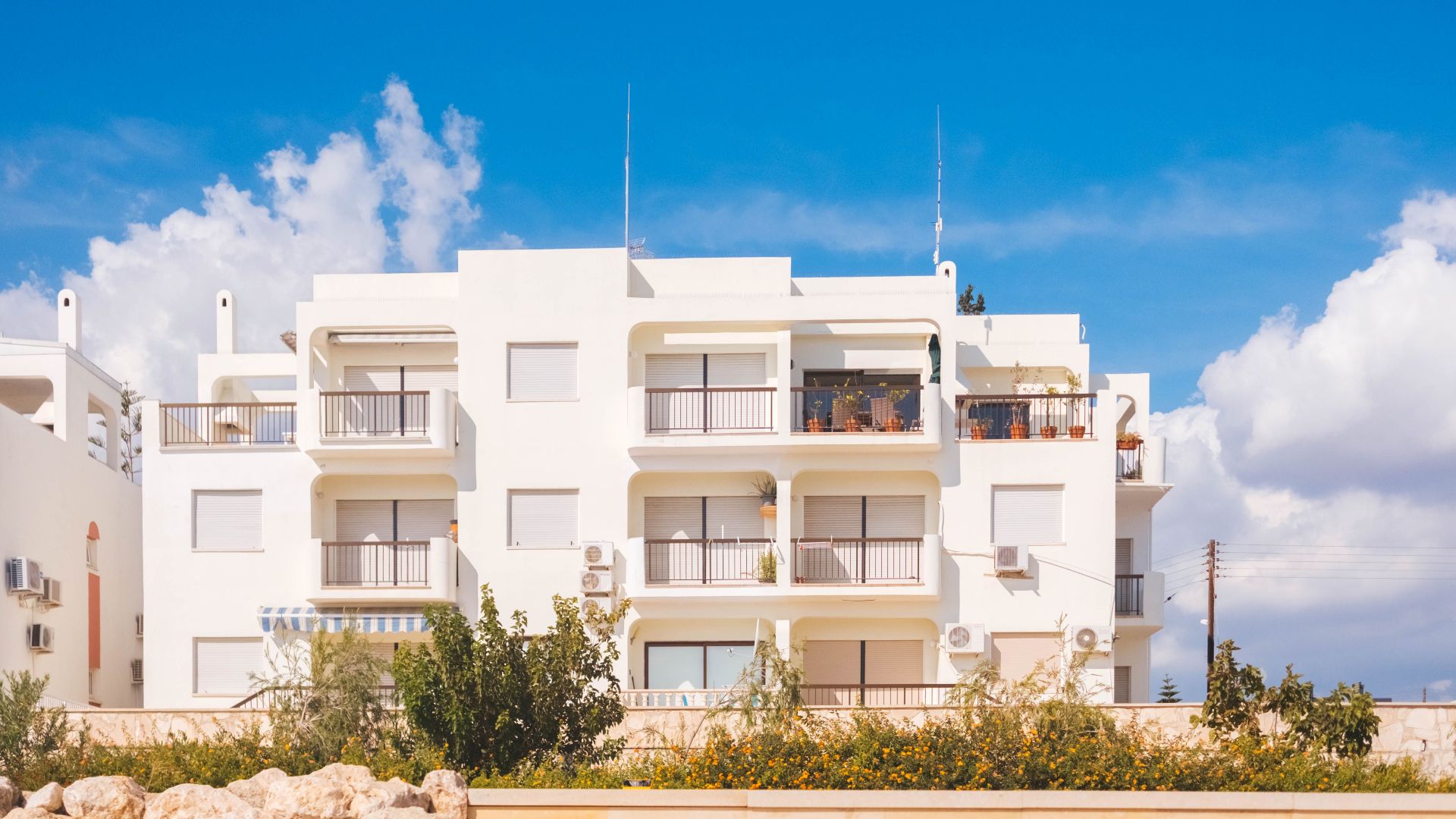 Stylish white apartment building exterior with balconies under a vibrant blue sky, showcasing modern architectural design.