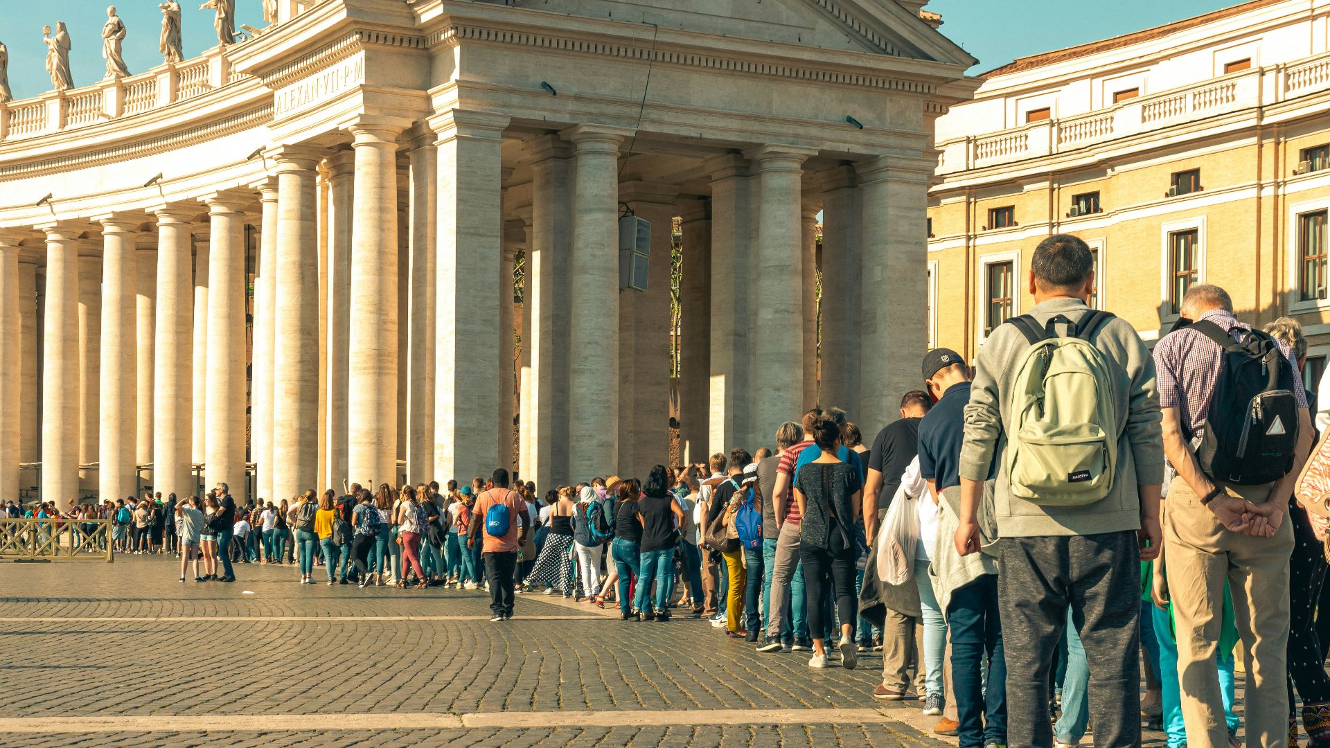 Tourists queue in front of a grand colonnade building.