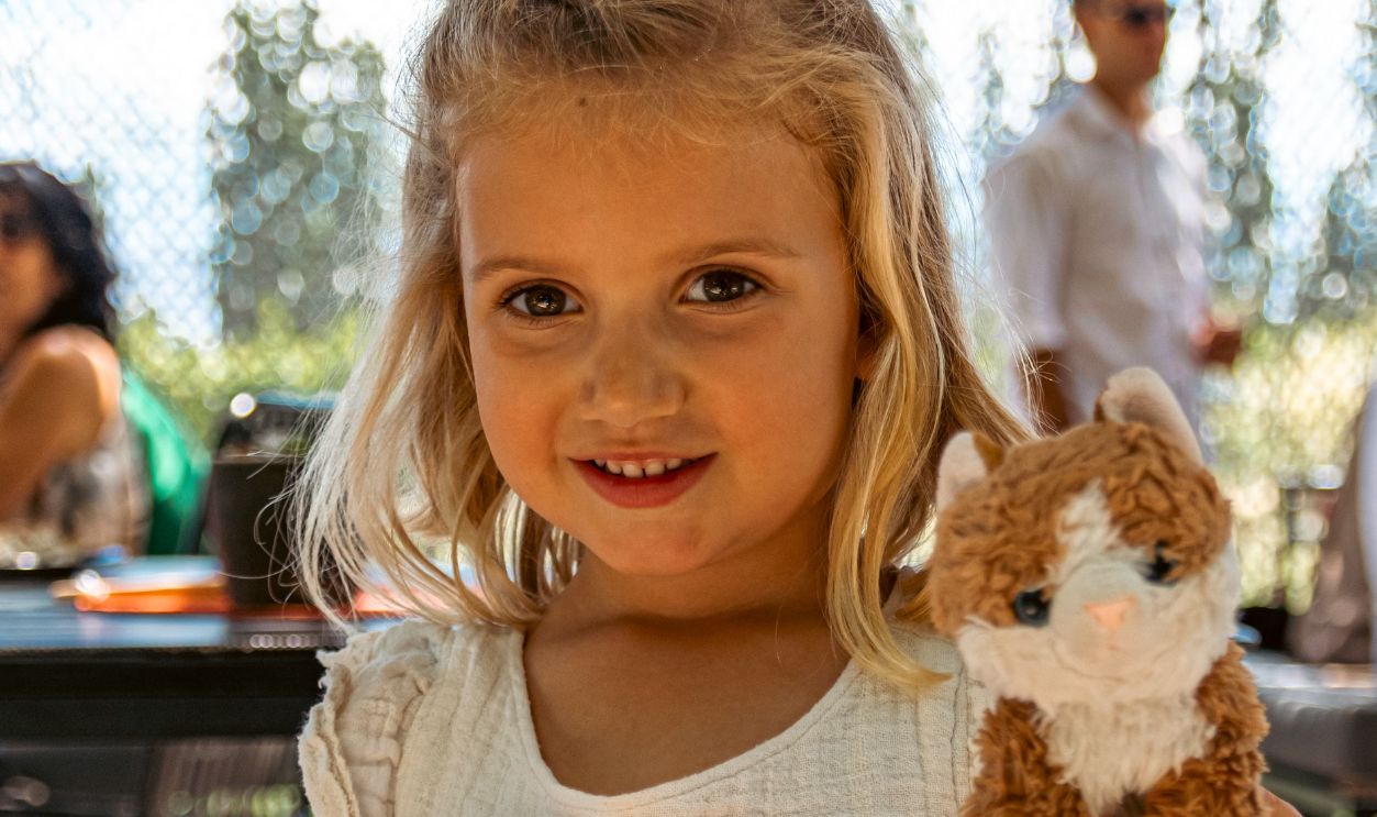 Adorable young girl in white dress holding a plush cat outdoors on a sunny day