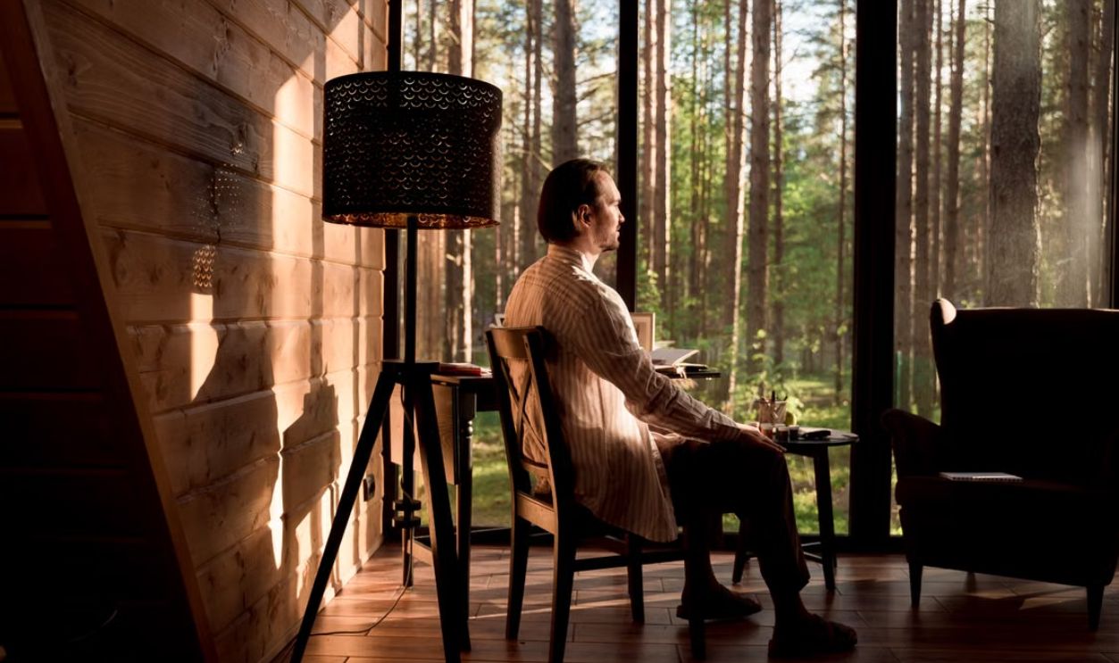 A man sitting in a serene forest cabin interior, enjoying the tranquil view outside