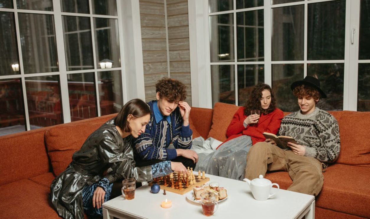 A group of friends enjoying a cozy indoor evening, sipping drinks and playing chess together.
