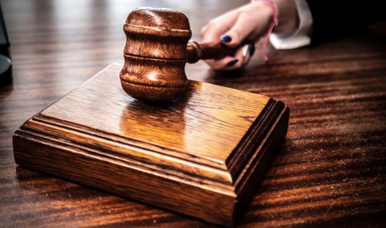 Close-up image of a wooden gavel held by hand on a desk in a courtroom setting