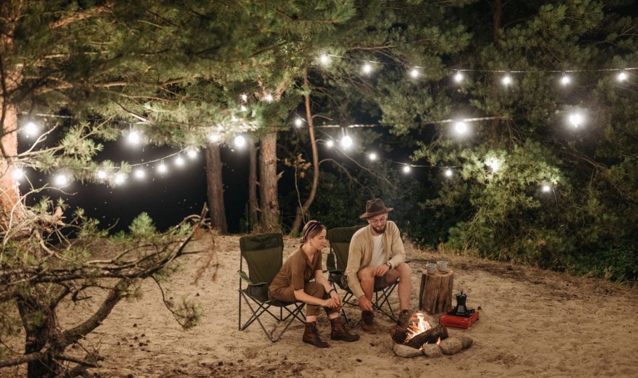 Couple enjoying a quiet night camping with a campfire and string lights in a forest setting