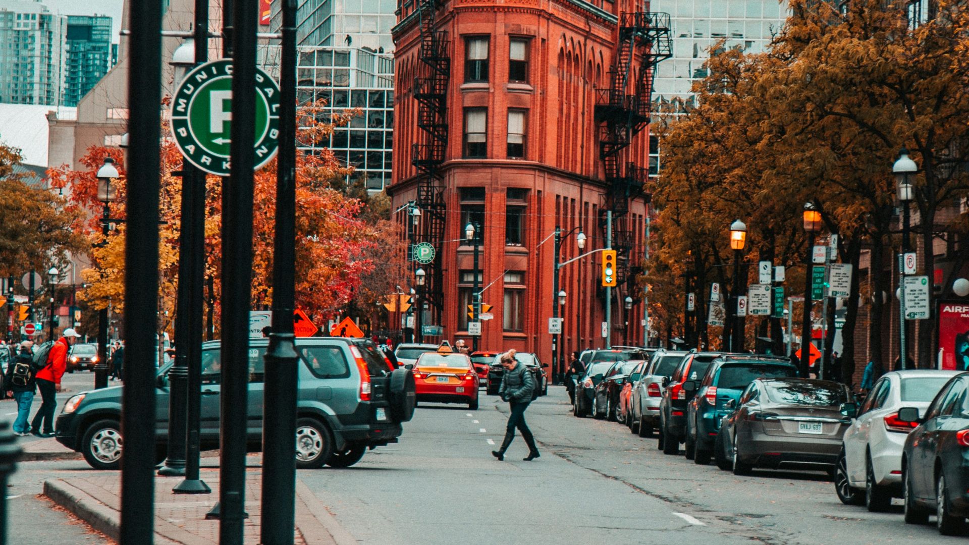 person crossing the road with parked cars beside the red building during daytime