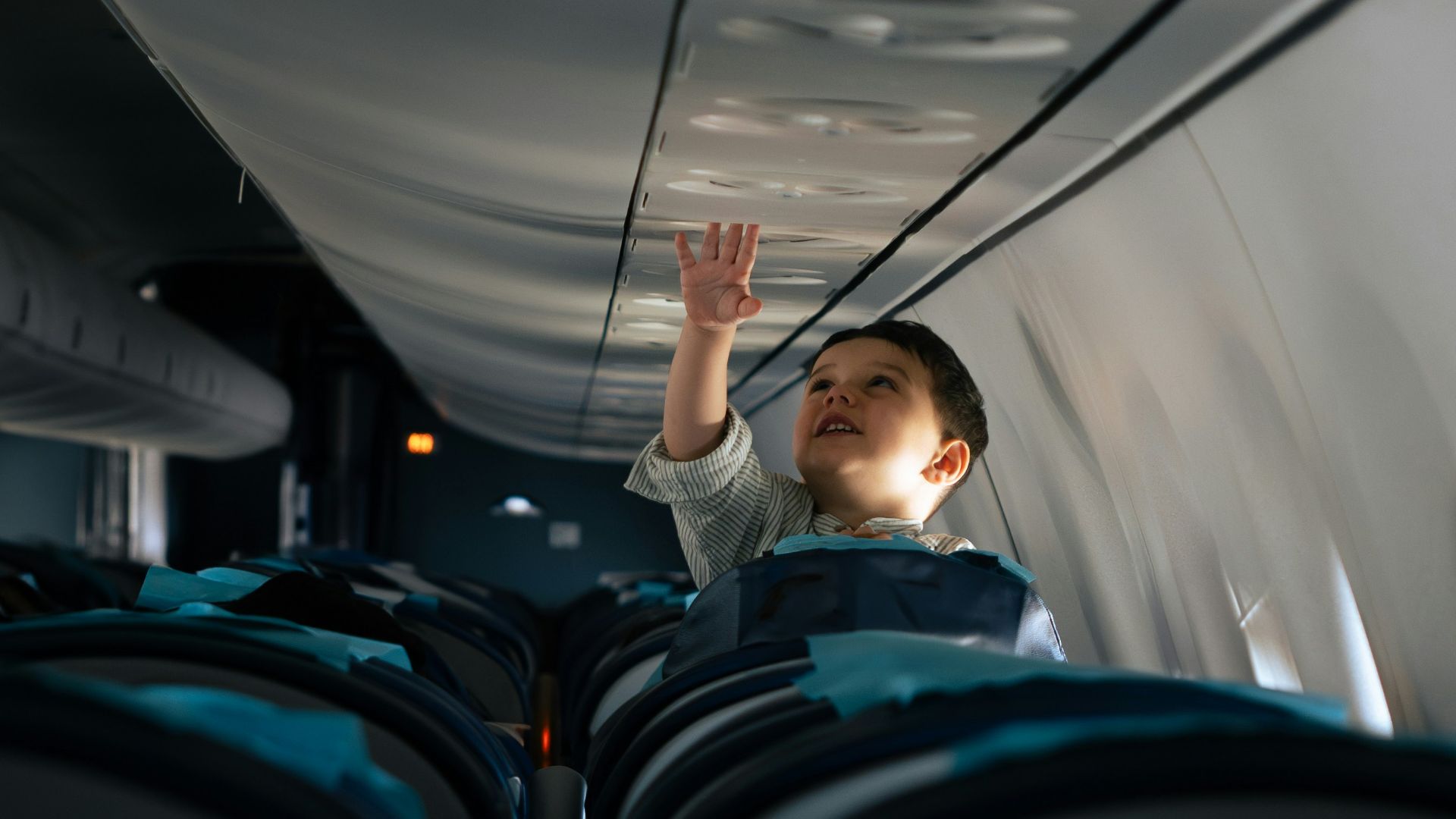 A child reaches for something on the airplane ceiling.