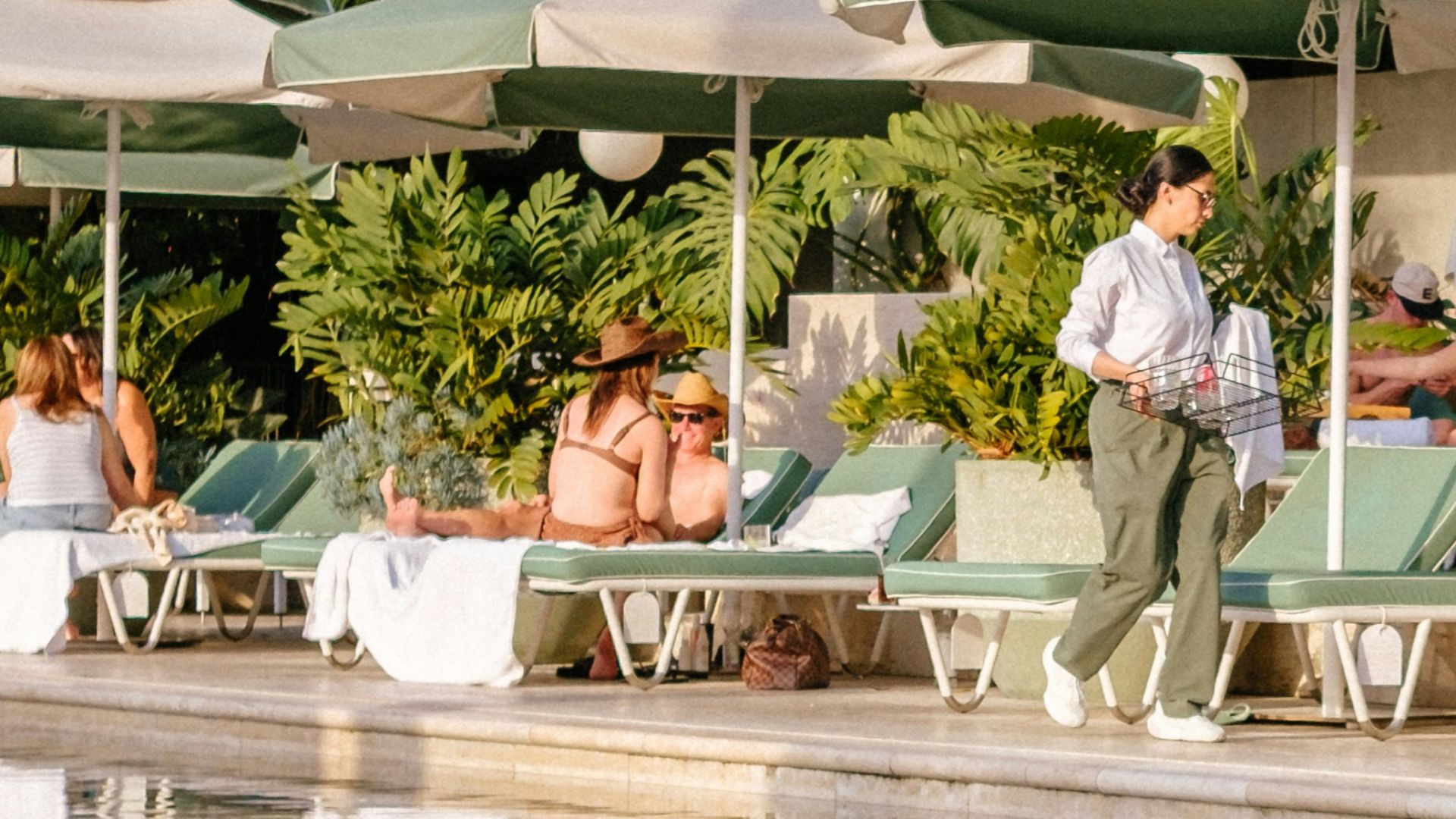 People relaxing by a resort swimming pool with lounge chairs.
