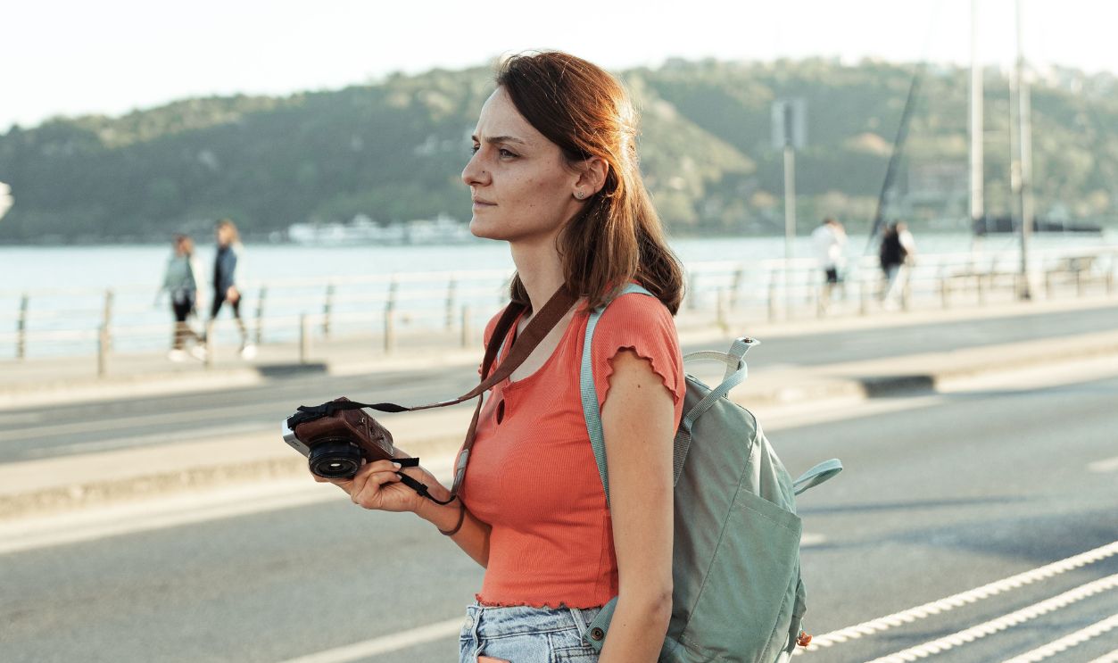 Woman standing by the waterfront with a camera and backpack