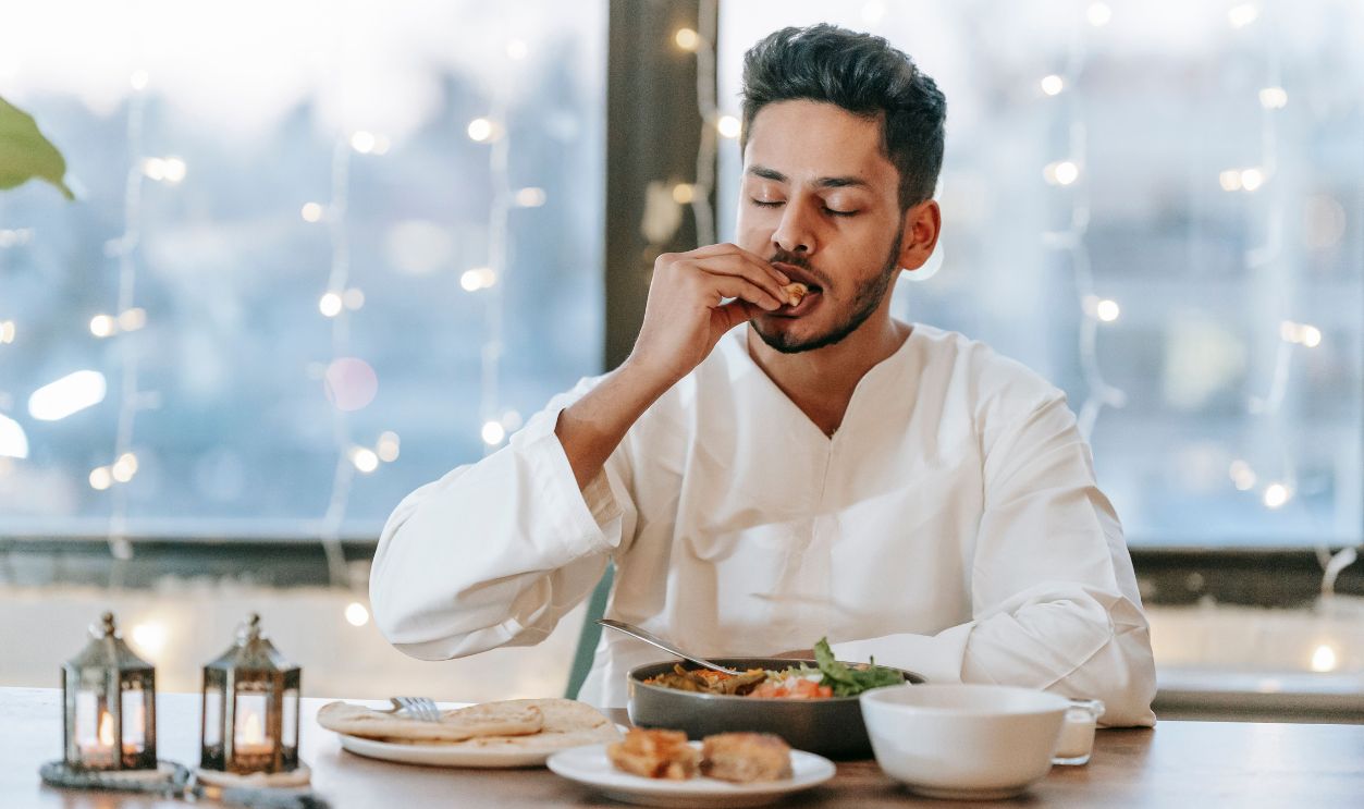 A man in a white thobe savoring a traditional meal indoors with string lights