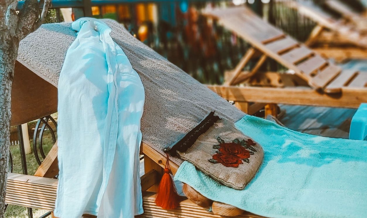 A peaceful outdoor scene featuring a sunbed with a white shirt and a pillow beneath a blue canopy
