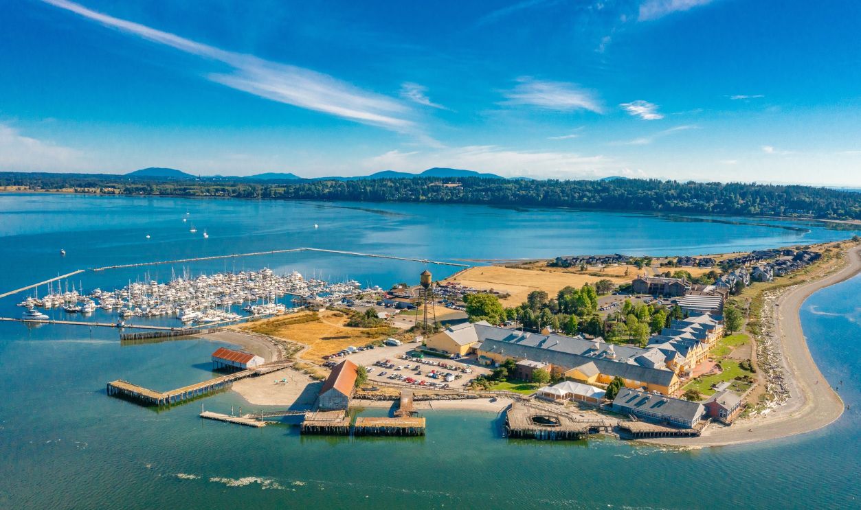 Drone photography of a group of condominiums on Semiahmoo in Blaine WA ocean on both sides view of Mt. Baker and an old water tower and marina full of sailboats and yachts