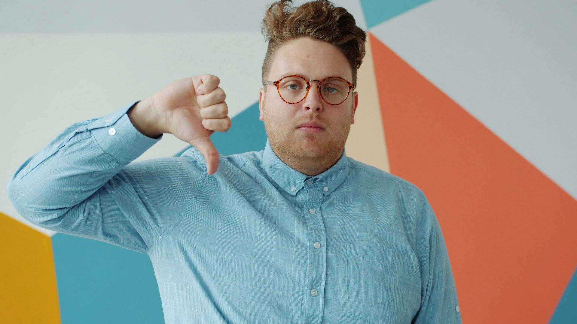 Man with glasses gives a thumbs down gesture.