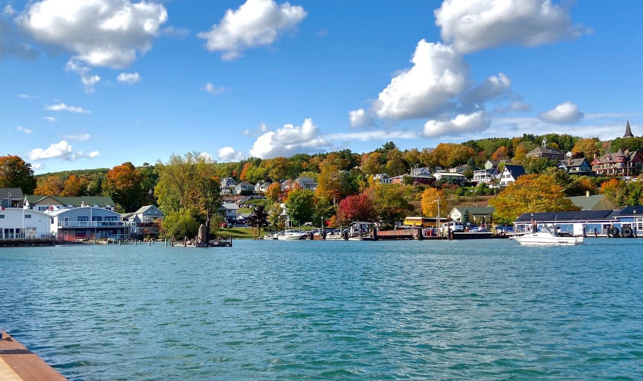 A stunning autumn landscape captured near Bayfield, Wisconsin, where vibrant fall foliage in shades of red, orange, and yellow contrasts beautifully against the deep blue-green waters of Lake Superior