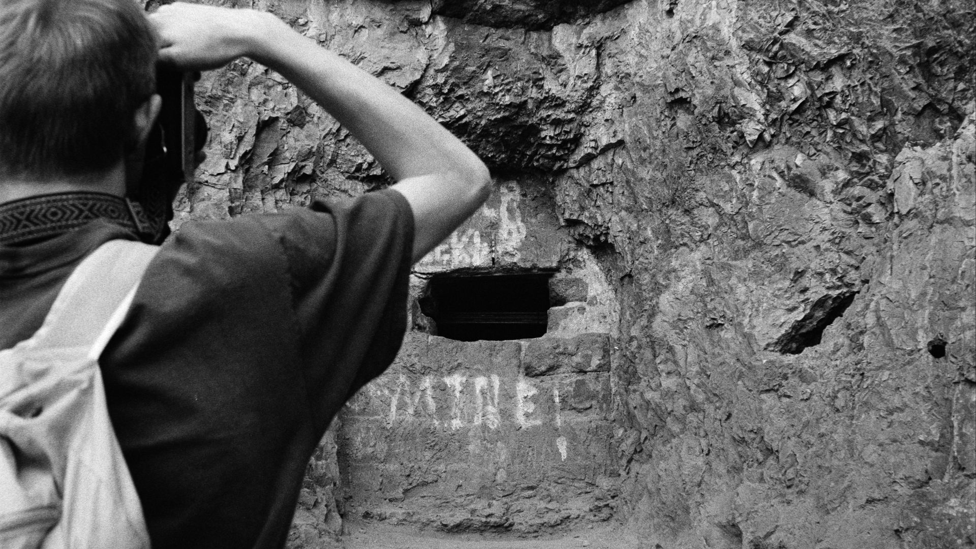 Man taking a picture of a cave entrance.