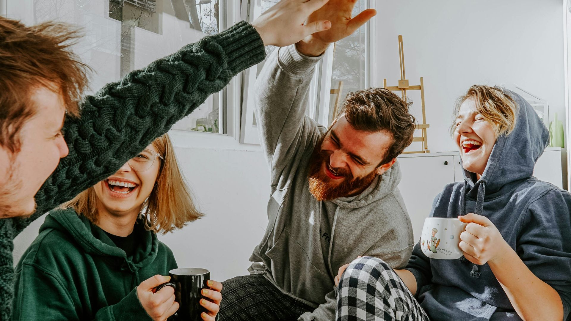 four friends laughing and high fiving over coffee