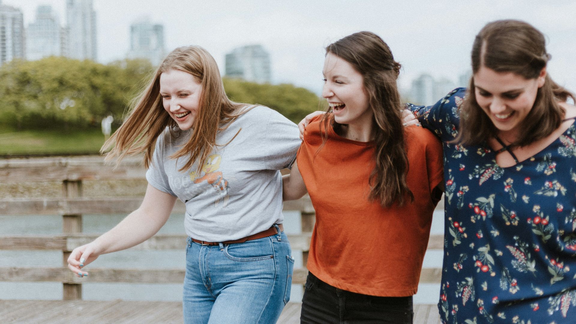 three women walking on brown wooden dock near high rise building during daytime