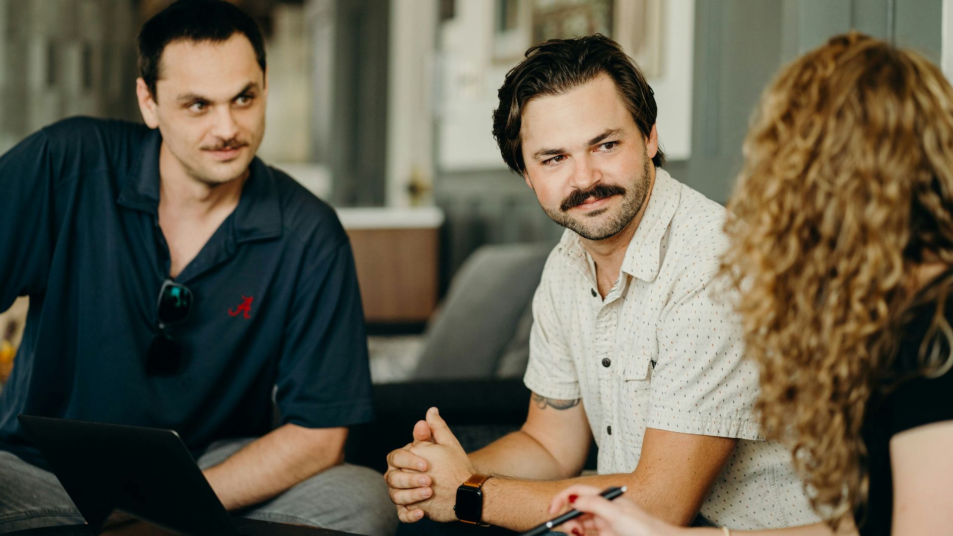 two men and a woman sitting at a table with a laptop