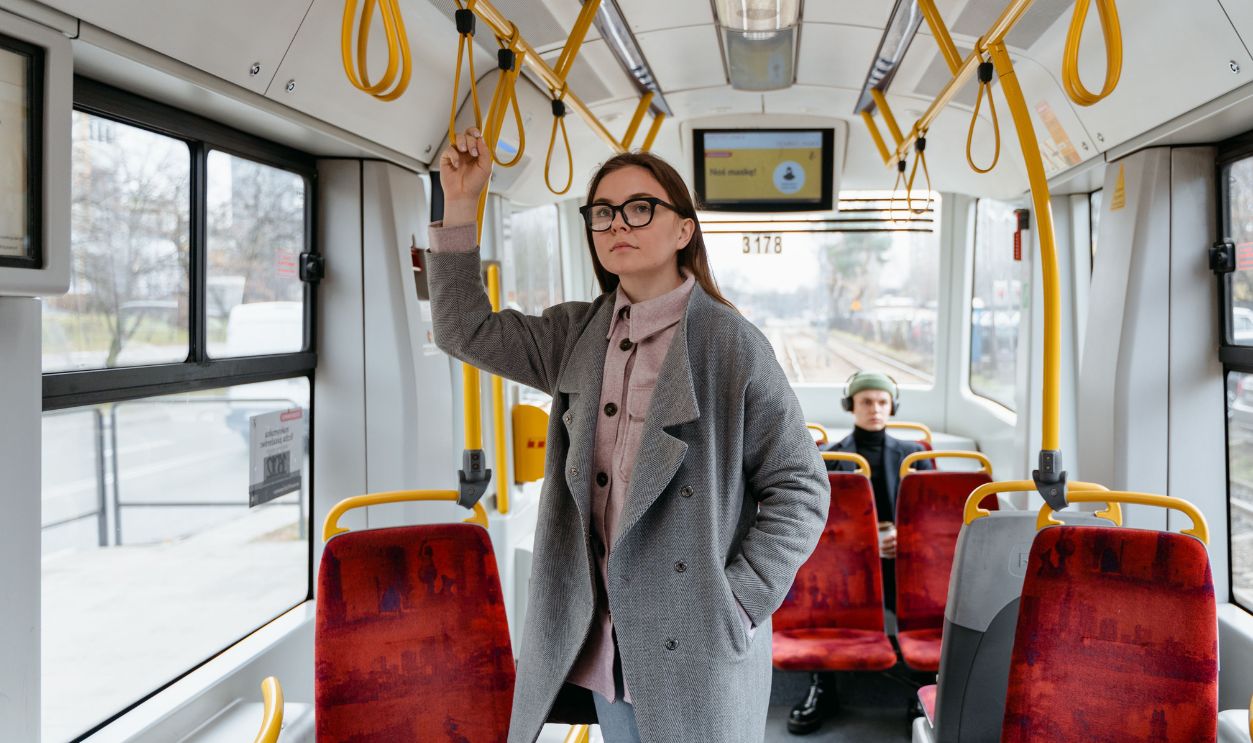 A woman in a coat and eyewear standing inside a public tram