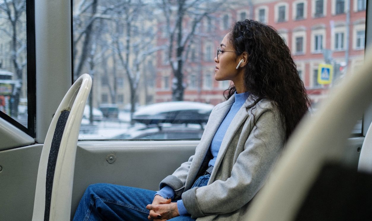 A woman wearing earphones gazes out the window of a bus